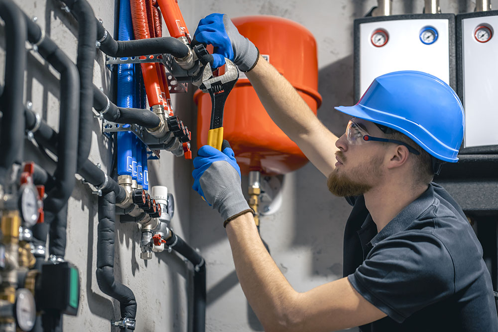 A man installs a heating system in a house and checks the pipes with a wrench. Adjusting heating valves in a residential building. A plumbing and heating technician works.